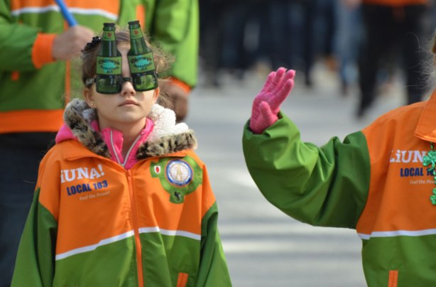 a young girl with a liuna union jacket on walks in a parade. she is wearing beer bottle shaped glasses