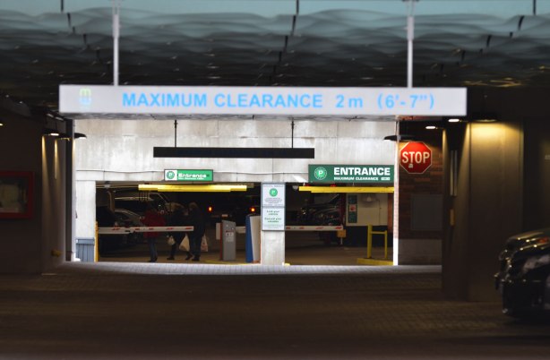 looking through a parking garage to a lighted entrance with people carrying bags and returning to their cars 