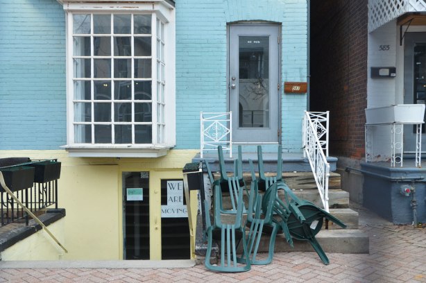 a pile of green chairs in front of the steps up to a pale blue building, lower level is painted yellow. 