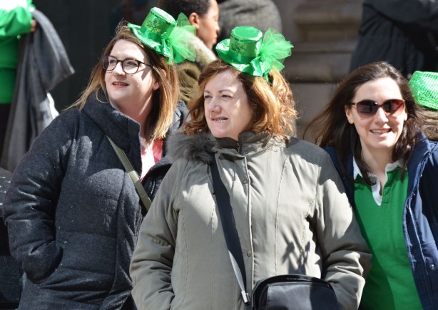 two women with little green hats perched on their heads watch the St. Patricks Day parade