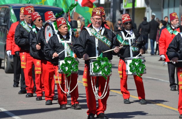 Ramses shriners band marches and plays in the St. Patrick Day parade. Red trousers, black jackets, large green shamrocks decorating their drums