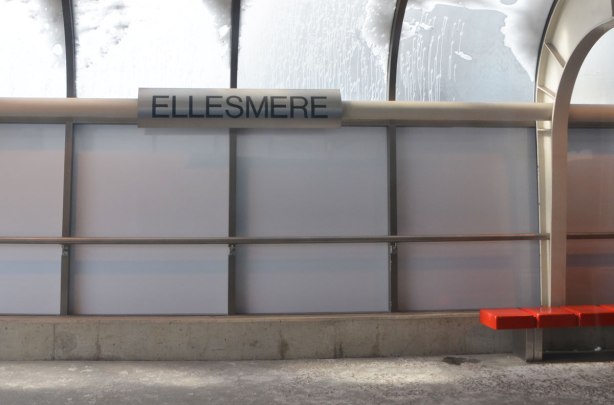 interior wall of Ellesmere station, covered (plastic?) glass wall, large black letters saying Ellesmere, and a bright red bench, snow on the curved translucent roof 