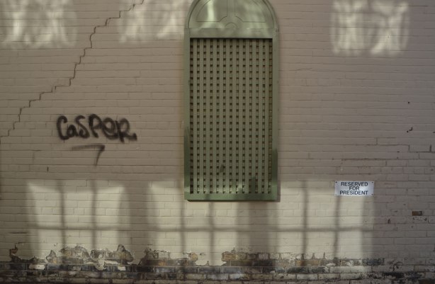 beige wall with greenish covering over a window, light reflected from the building beside it makes it look like a row of windows along the wall
