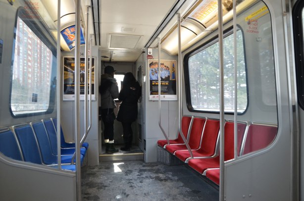 looking down the length of an SRT car, two young women are looking out the back window. seats down either side, red on one side and blue on the other