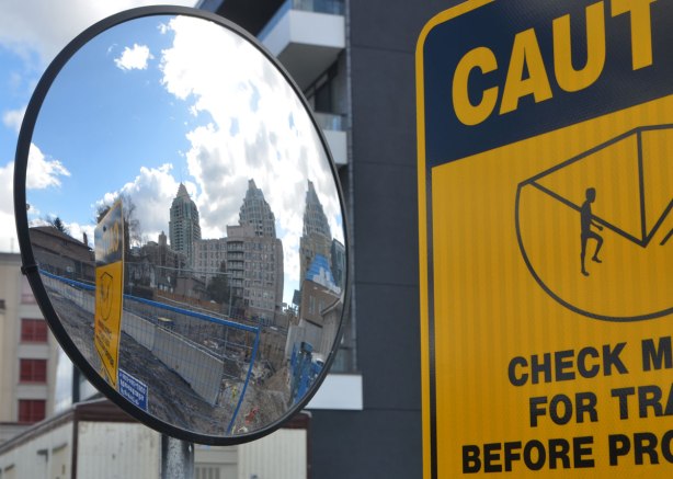 a convex mirror beside a black and yellow caution sign, condos are reflected in the mirror 