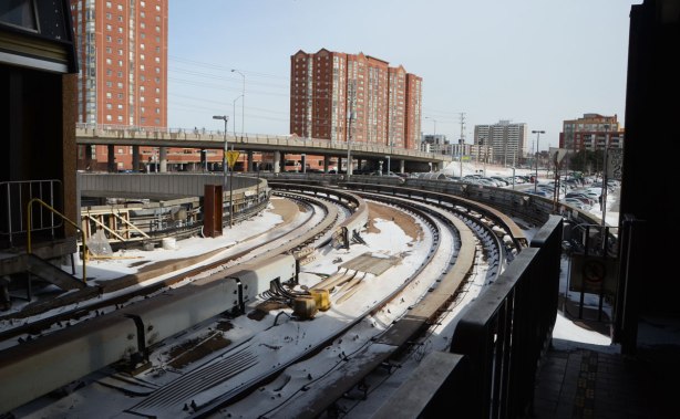 SRT tracks curve away from platform, outside, apartment building in the background, some snow on the tracks 
