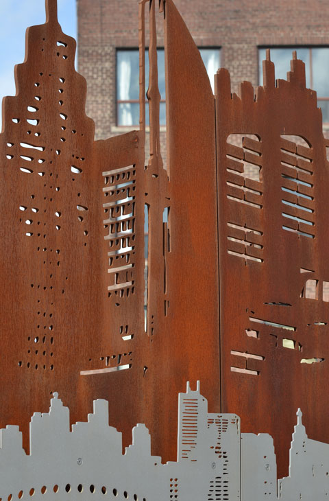 rusted metal cut out, part of a public art installation, cut outs look like houses, polished steel cutouts below the rusty ones. 