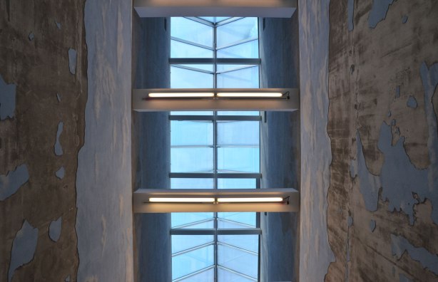 looking upwards to a skylight two storeys above, the walls of the narrow room (hall) are covered with plaster and painted light blue with clouds, some of the plaster is peeling away and it's supposed to look like the sky is falling 