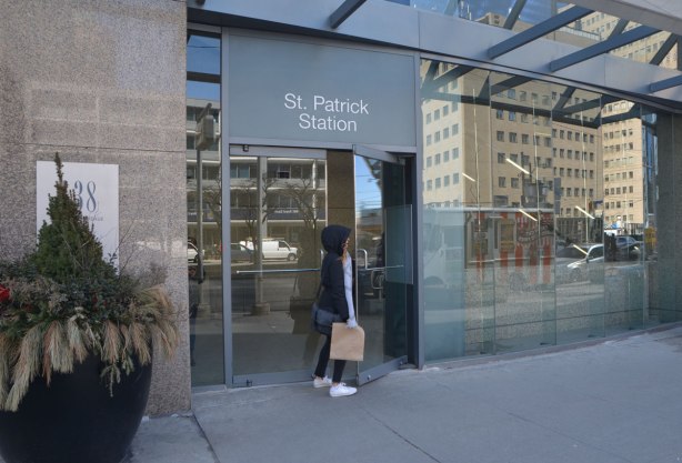 a woman is opening the glass doors of St. Patrick station, at street level, on University Ave