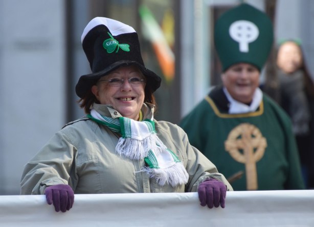 a woman with a big smile and wearing purple gloves is holding up a white banner in a parade