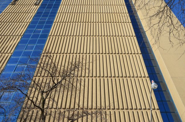looking up a building with strong vertical lines made by concrete shapes on theglass is reflecting strong blue colour exterior of the building,