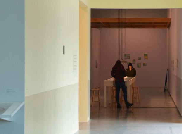 two women looking over a table with art displays on it , in an art gallery