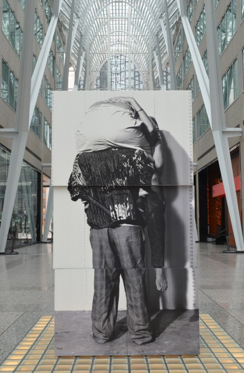 photographs of the back of a person with another person sitting on his shoulders, upper person is leaning forward with head down, the blocks on which the photos are printed are in the walkway at Brookfield Place