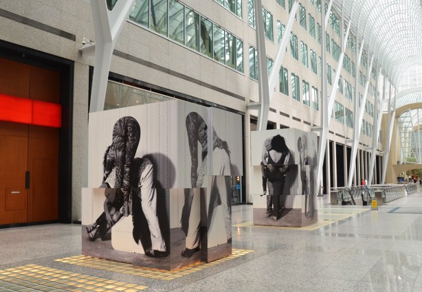 two large cubes constructed from pieces of photos of different people in different positions sit in the middle of Brookfield Place, under the glass arched roof. 