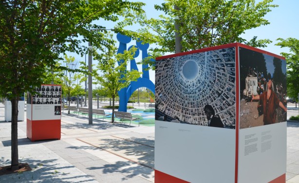 an outdoor art exhibit on peace, two of the structures used for mounting pictures on, with the blue sculpture on Front Street, Canaray District, in between the two boxes. 