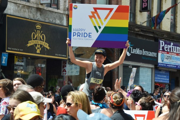a woman is on another person's shoulders so she's above the crowd walking in the dyke march. She is holding a sign that says happy pride