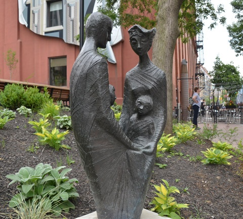 sculpture of a family - father, mother and child in a park, with new garden plantings around it, hostas mostly