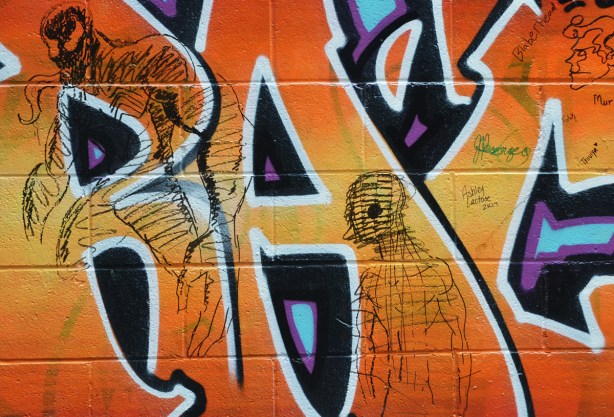two figures, drawn abstractly with black marker on top of orange street art, 