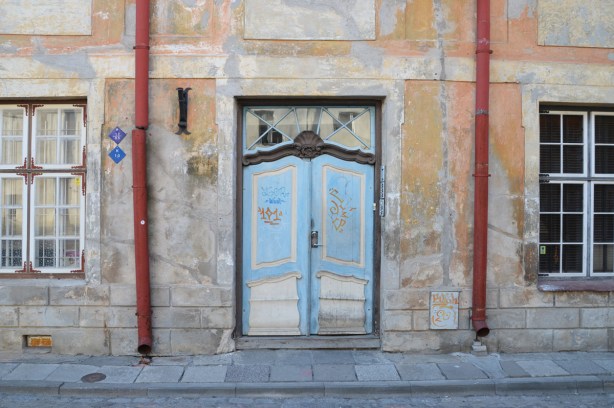 front door of a house in Tallinn Estonia, wood, blue and white double doors, orange faded paint on the concrete facade, 2 red drain pipes run down the front, one on each side of the door 