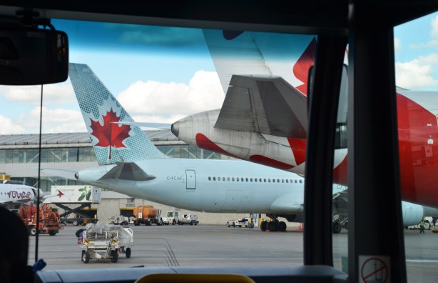looking through the front window of a bus as it drives on the tarmac behind aiplanes parked at gates 