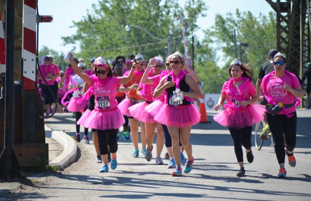 a group of women running in the Run Like a Diva run, all in pink tutus and many in pink t-shirts, laughing and cheering as they come close to the finish line in their pink boas and tiaras