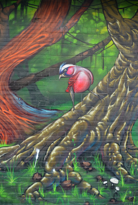 part of a large colourful mural by clandestinos smoky and shalak - a small bird on the base of a tree trunk