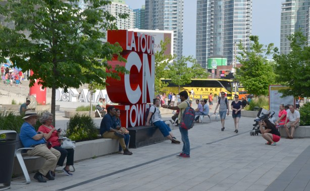 3D sign for the CN tower with tourists taking pictures in front of it. Canada 150 3D sign in the background as well as some people sitting around on benches 