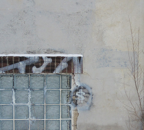 grey concrete wall with window, someone has drawn a dollar sign on the wall, leafless shrub growing against the wall, winter time 