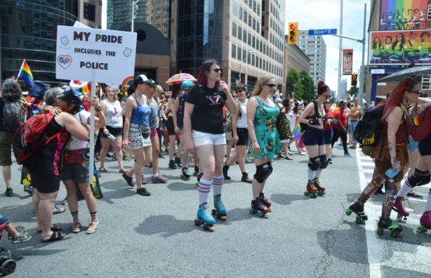people on roller blades at the start of the dyke march. a woman holds a sign that says my pride includes the police