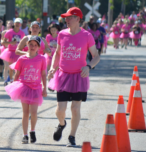 a father and daughter, both in pink tutus run in a 5k race, Run Like a Diva, other runners in the background 
