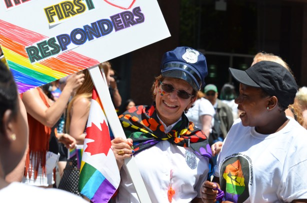 a woman in rainbow scarf, and police hat, holds a sign that says thanks first responders