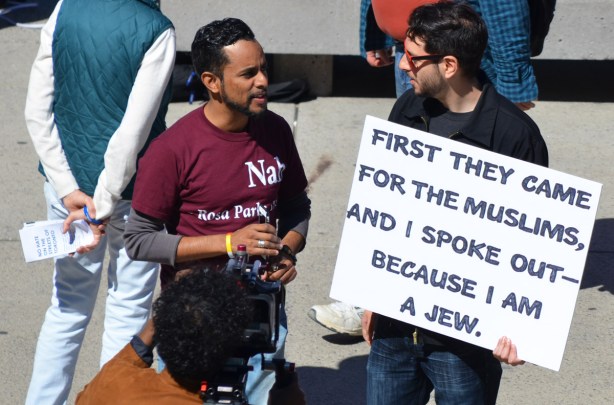 two men talking at a protest rally. one holds a sign that says First they came for the muslims and I spoke up because i'm a Jew