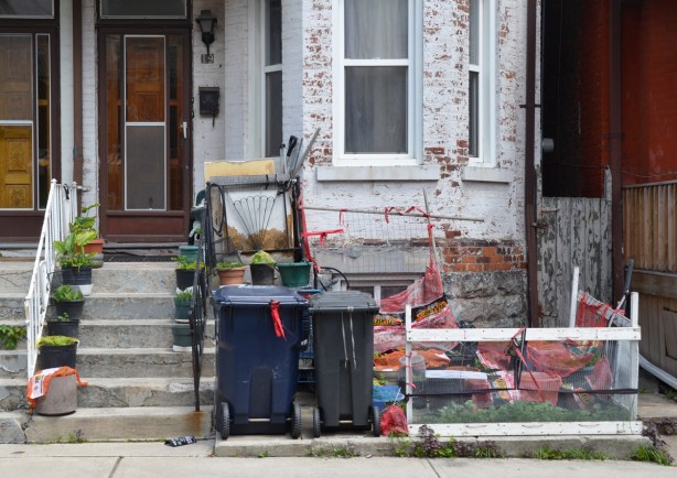 a front yard with gardening supplies, and pots of plants on the front steps 