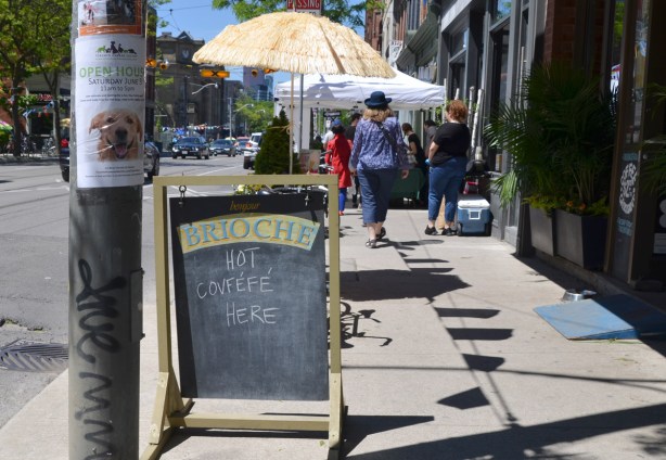 a blackboard sign on the sidewalk in front of Brioche restaurant that says we serve Covfefe. People walking on the sidewalk, 