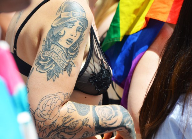 torso from the side of a person in a lacy black bra with a large tattoo on upper and lower arm. Upper arm tattoo is a woman's head with the words live deliciously written under it 