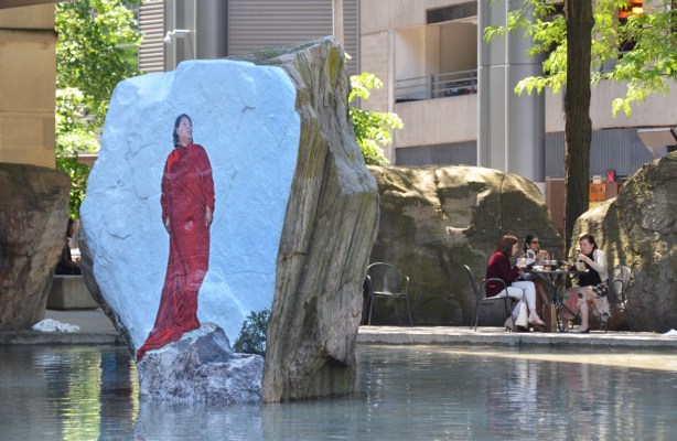 photograph or painting of a woman in red standing on a rock, directly onto the surface of a large rock in a shallow pool of water