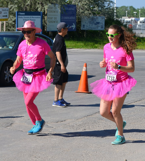 a man is dressed in pink for the Run Like a Diva event, pink wide brimmed hat, pink t-shirt and pink tights as well as pink tutu. Bright blue shoes. 