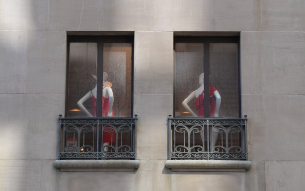 two mannequins with their backs to two windows, both dressed in red clothes
