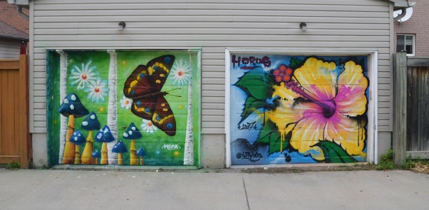 a mural on a garage door in an alley, part of butterflyways project - two adjacent garage doors, the left one is by mska and is a brown butterfly and mushrooms. on the right is an hibiscus flower by horus taffytats