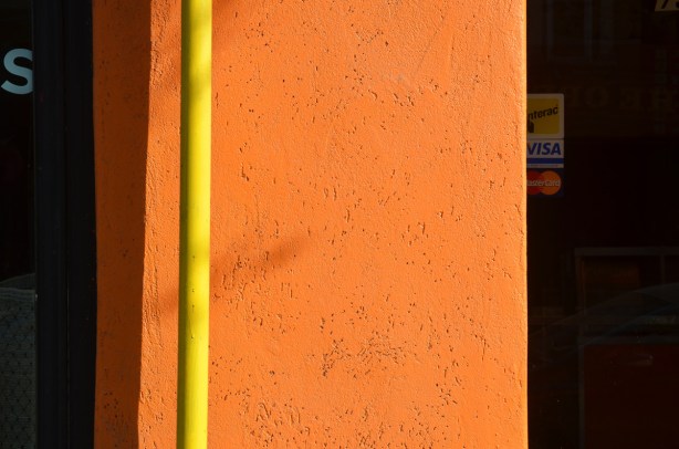 bright yellow pipe against a bright orange wall, with shadow. 