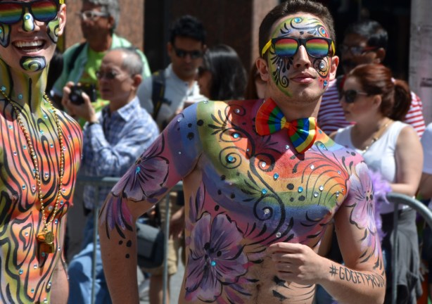 two men with a lot of bodypaint of rainbows and flowers as well some sparkly bits 