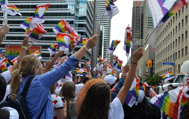 lots of people with arms up in the air waving small rainbow flags