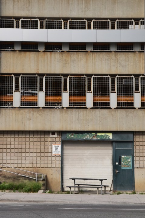 parking structure on the top, old door and wall on the bottom. A wood picnic table in disrepair is in front of the door 