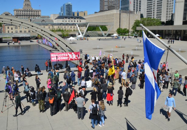 lookng down from the upper level, people at a protest rally at Nathan Phillips square, Toronto flag in the foreground
