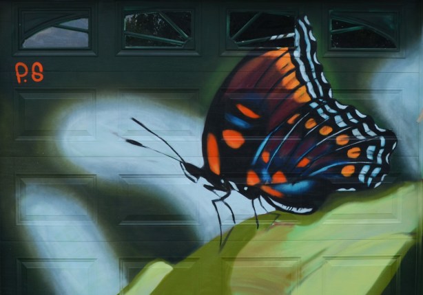 a mural on a garage door in an alley, part of butterflyways project - a black butterfly with orange and blue highlights, on a green leaf