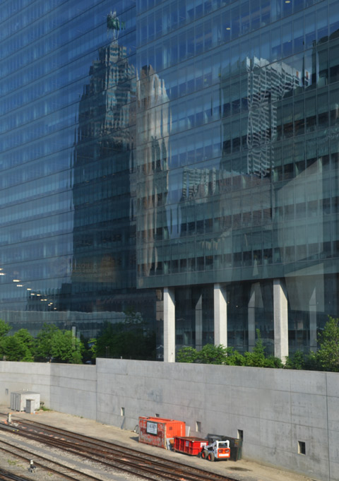 buildings reflected in another glass building right beside the trains tracks south of Union Station