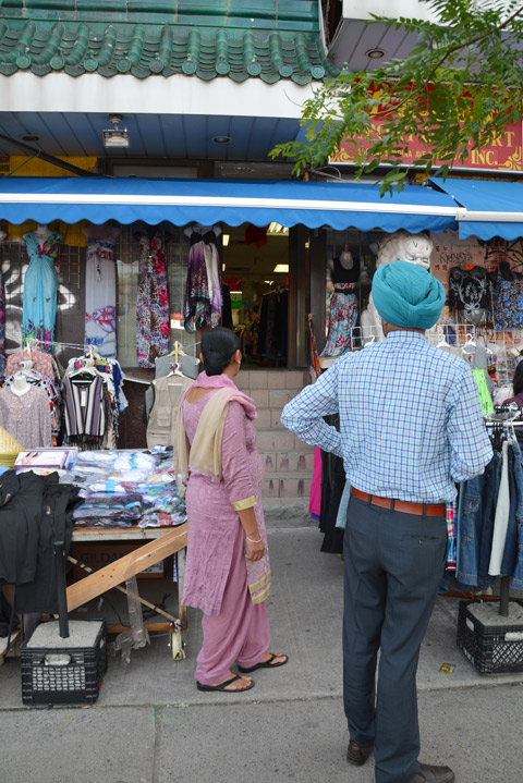 a woman in a pink saree and a man in a turquoise turban stand outside the entrance to a clothing store on Spadina 
