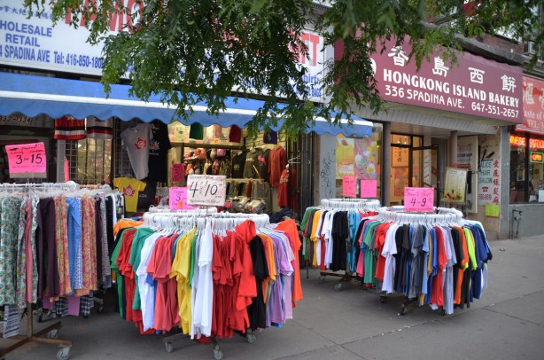 racks of pants and t-shirts for sale, on the sidewalk outside a store
