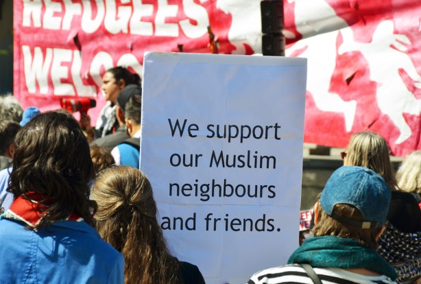 people at a protest rally, one is holding a sign that says We support our Muslim neighbours and friends