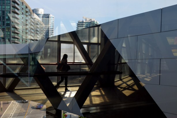 reflections of a woman walking on the Skywalk between Union Station and the convention center, with views of the street below and buildings beyond also in the frame